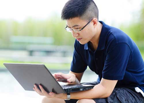 Millennial man, glasses, blue polo shirt, using laptop to learn about term life insurance quotes.