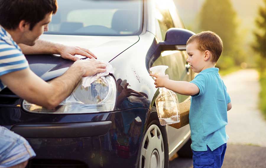 Father and son cleaning and maintaining their high mileage car in the drive way.